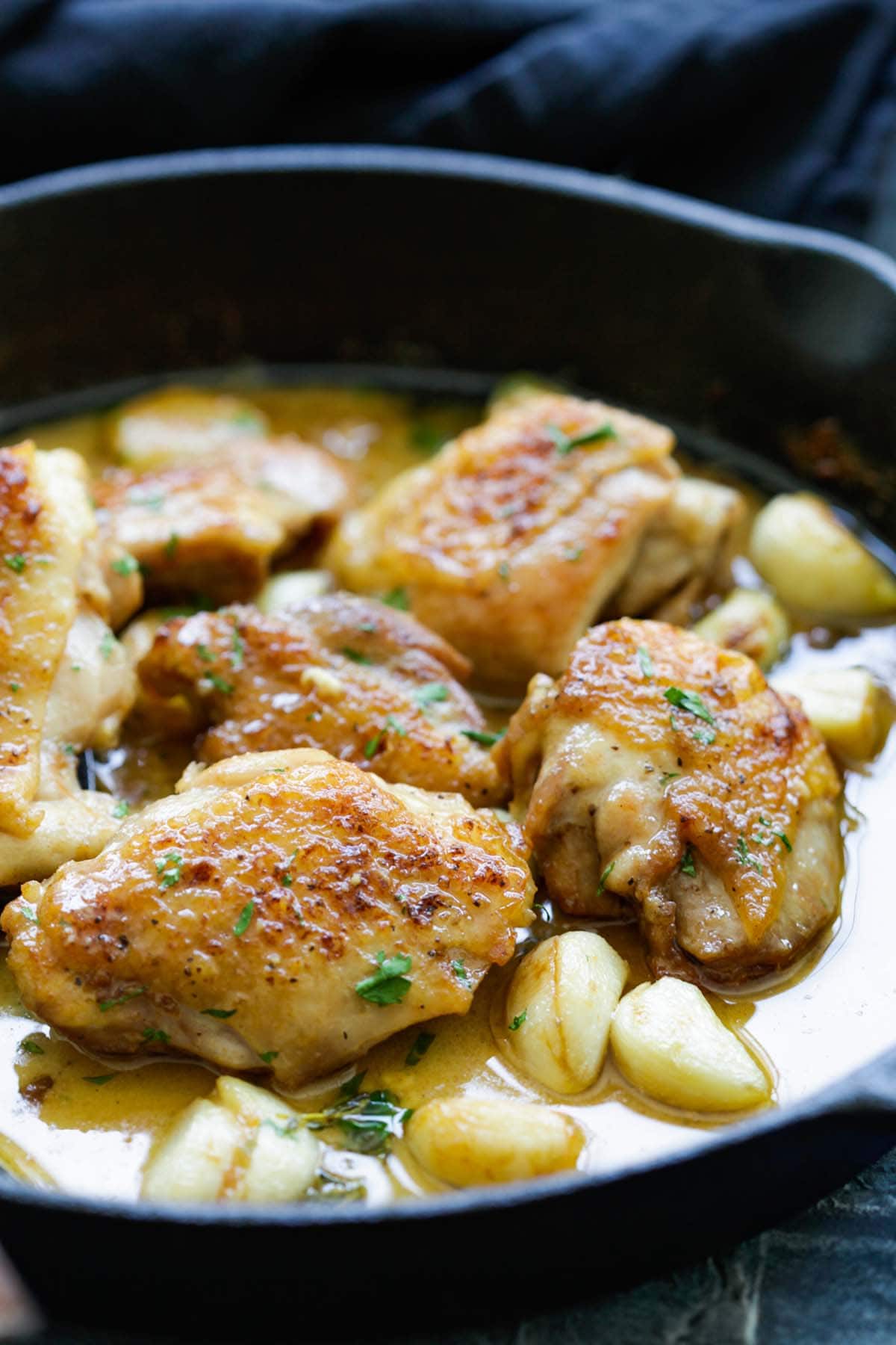Garlics and chicken thigh with creamy sauce in a cast-iron skillet.