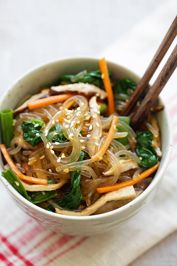 Korean Japchae with sweet potato noodles and vegetables in a bowl with a pair of wooden chopsticks.