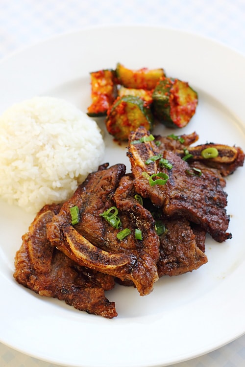 Delicious kalbi or Korean short ribs on a plate with rice and spicy cucumber salad. Try this recipe at home today.