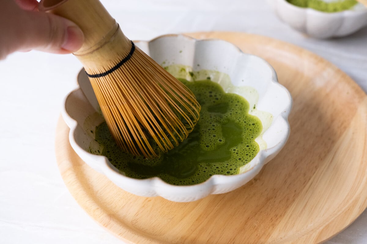 Matcha powder dissolving with hot water in a small bowl. 