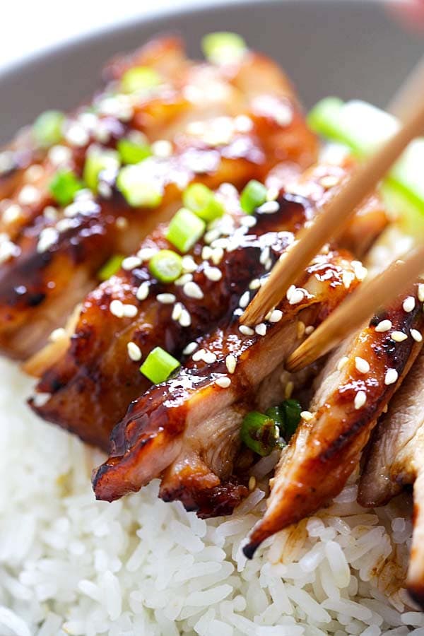 Tasty soy-glazed chicken on top of steamed rice garnished with chopped scallions and sesame seeds, ready to serve.