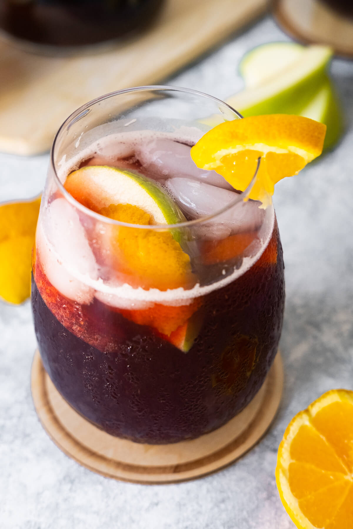 Sangria in a glass with apple and orange slices and a piece of orange on the slide of the cup.
